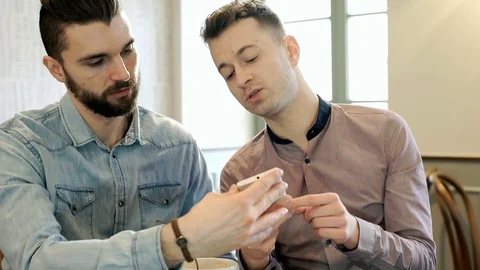 Two men sitting in the cafe and looking on smartphone, steadycam shot Video stock 73437976