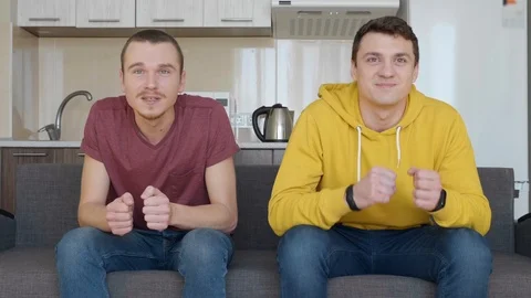 Two men sitting on the couch and watching decisive moment of football match Video stock 107649331