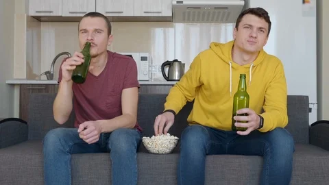Two men sitting on the couch watch a football match on TV, drink beer Stock Footage 107649234