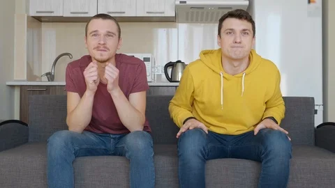 Two men sitting on the couch watch a football match on TV and enjoy the victory Stock Footage 107649895