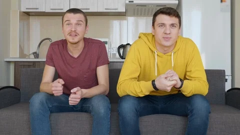 Two men sitting on the couch watch a football match on TV Stock Footage 107650163