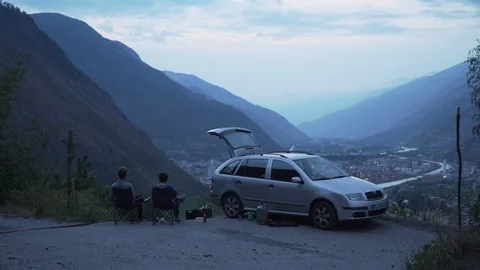 Two men sitting in deck chairs besides car, toasting with a beer, 4K Stock Footage 129612792
