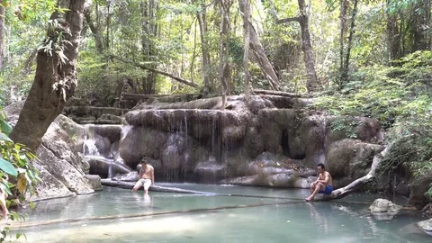 Two Men Sitting On Fallen Log at a Small Waterfall in the Jungle Stock Footage 74292067