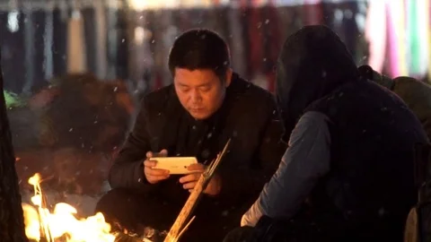 Two men sitting by fire to keep warm from light snowfall in China, Shenyang 스톡 동영상 84756729