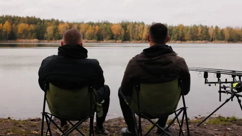 Two men sitting on folding chairs by the lake during autumn fishing, falling Stock-Footage 319484934