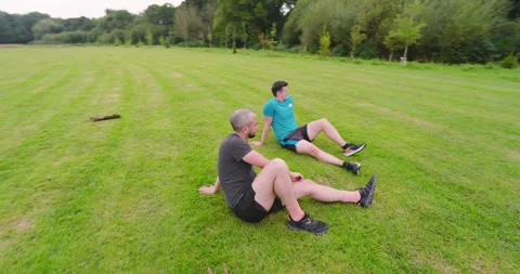 Two men sitting on grass in park, resting after jogging in nature Stock Footage 345571398