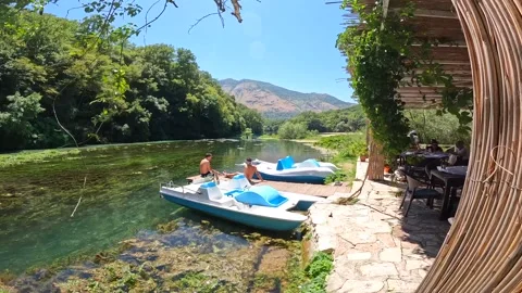 Two men sitting next to some pedalos in the river of The Blue Eye or Syri i.. Stock Footage 248537997