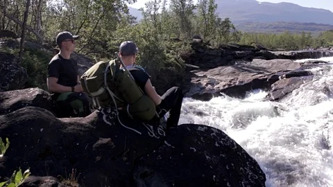 Two men sitting by a rapid river Stock Footage 97201338