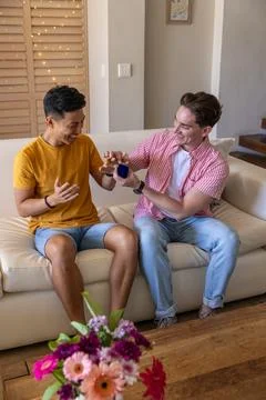 Two men sitting on sofa in living room, presenting navy-blue ring box, wearing Stock Photos