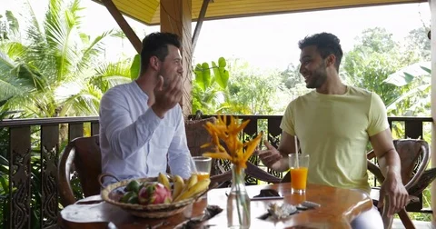 Two Men Sitting On Summer Terrace Talking Drink Orange Juice, Mix Race Gay Stock Footage 77586699