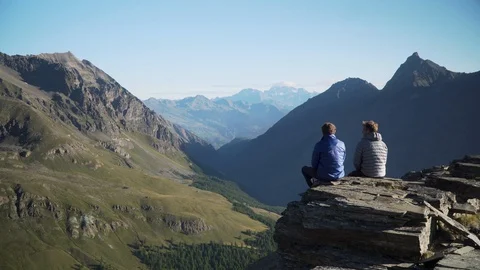 Two men sitting together on rock and looking at mountain panorama, 4K Stock Footage 129612572