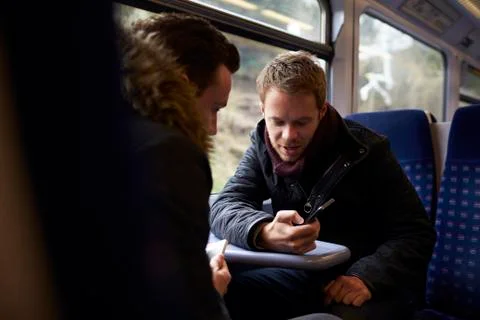 Two Men Sitting In Train Carriage Looking At Text Message Stock Photos