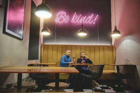 Two men sitting under a neon 'Be Kind' sign in a craft beer bar Stock Photos
