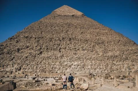 Two men stand in front of old pyramid with their pants down. Stock Photos
