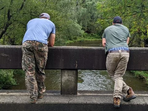 Two men stand on the side of a bridge looking over a forest creek Foto stock