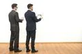 The two men stand with a tablet and papers on the white wall background Photo