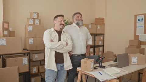 Two men standing with arms crossed beside cardboard packages in a packing b.. Video stock 339215540