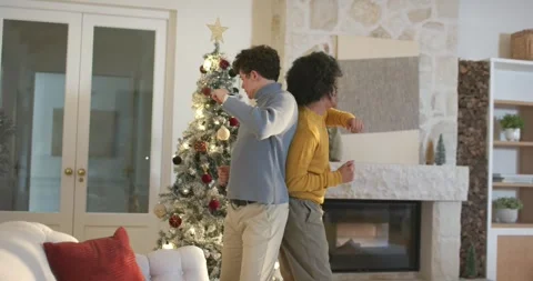 Two men standing back-to-back in living room by lit Christmas tree, moving then Stock Footage 344656601