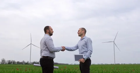 Two men standing in a field with wind turbines in the background Stockbeeldmateriaal 147086801