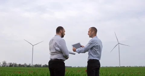 Two men standing in a field with wind turbines in the background Video stock 147091632