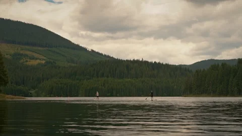 Two men standing on stand up paddle board sup water sport on a mountain lake Stock Footage 251796977