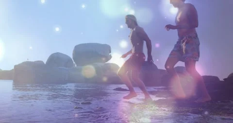 Two men stepping into surf reaching shallows and running with pink bokeh Stock Footage 331287168