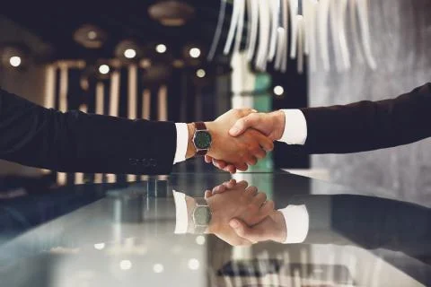 Two men in suits shaking hands over the black desk Stock Photos