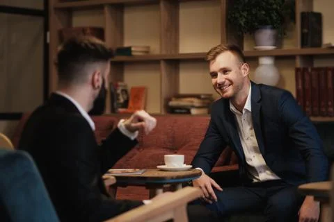 Two men in suits sit in a restaurant. A business meeting. Men drink coffee. Stock Photos