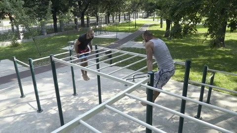 Two men synchronized doing chin ups on bars in park, street workout, gimbal shot Video stock 93858450