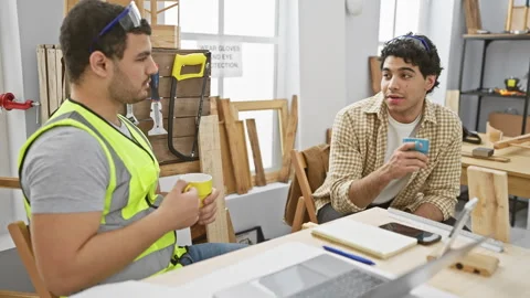 Two men take a coffee break in a bright carpentry workshop, discussing work.. Stock Footage 270314870