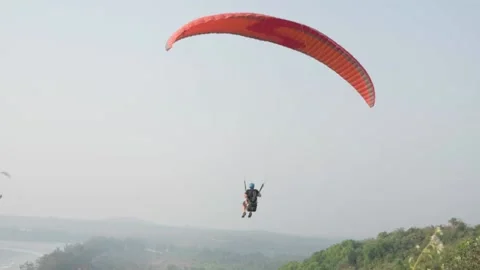 Two men take off in a paraglider from a mountain, and fly off into the distance. Stock Footage 228823992
