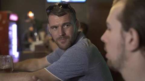 Two men talking and drinking beer in sport bar. Fiends sitting at bar counter 스톡 동영상 104387867