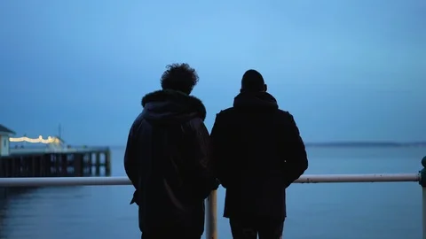 Two men talking and looking out at sea at dawn Stock Footage 114121495
