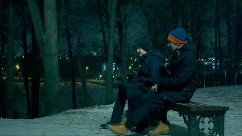Two men talking to each other and laughing at snowy winter night on the bench Stock Photos