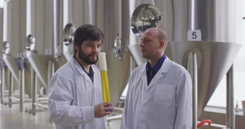 Two men testing quality of fresh beer in a brewery. Brewers dressed in lab coat Stock-Footage 148230823