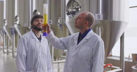 Two men testing quality of fresh beer in a brewery. Brewers dressed in lab coat Stock Footage 148231327