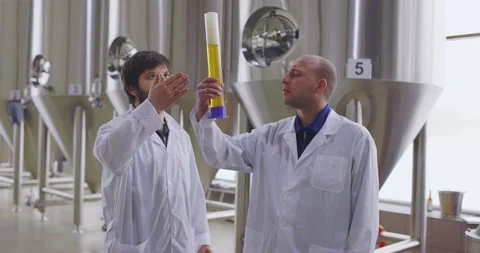 Two men testing quality of fresh beer in a brewery. Brewers dressed in lab coat Vídeos de archivo 148391392