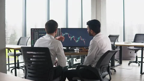 Two men traders sitting at desk at office together monitoring stocks data candle Video stock 234223987