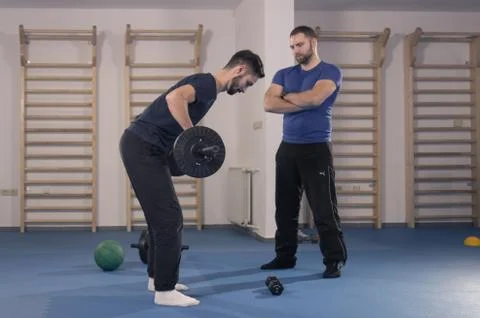 Two men, trainer instructor watching exercise, weights bar Stock Photos