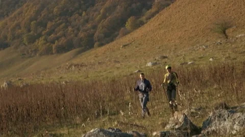 Two men with trekking poles are walking through the mountains Stock Footage 171637901