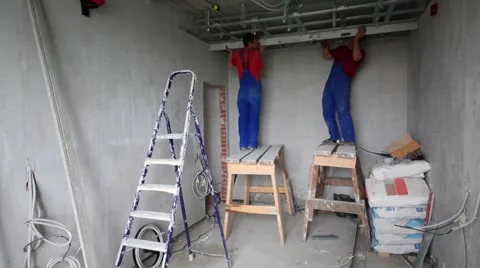 Two men in uniform install framework for hung ceiling in new flat Stock Footage 45230433