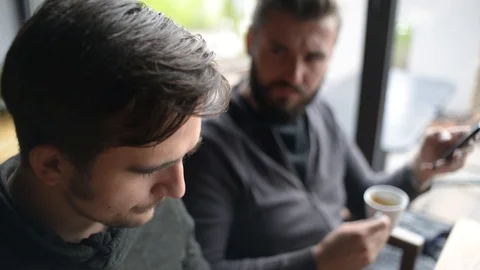 Two Men use Mobile Smart Phones in Hands during a Coffee Lunch in a Cafe Stock-Footage 95636477