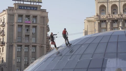 Two men using safety rope are cleaning glass roof of the building Stock Footage 127354367