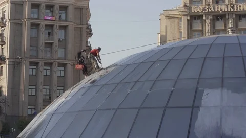 Two men using safety rope are cleaning glass roof of the building Stock Footage 127354708