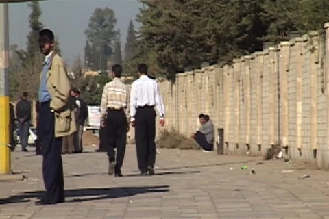 Two men walk away from camera. Others waiting to cross street and talking. Stock Footage 86753127
