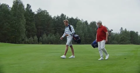 Two men walk the golf course with bags of clubs talking to each other Stock Footage 164394614