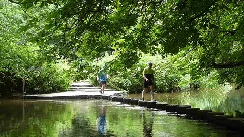 Two men walking across Stepping Stones in the river Stock-Footage 77384997