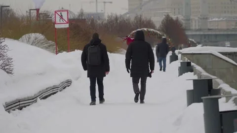 Two Men Walking Along Snowy City Riverfront Path in Winter Coats on Overcast Day Stock Footage 331237291