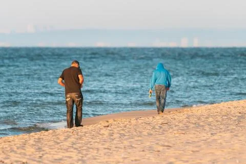Two men walking on a beach by Baltic sea away from the viewer on early summer Stock Photos