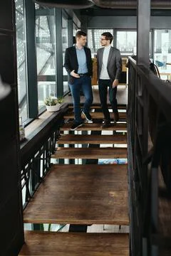 Two men walking down stairs chatting indoors Stock Photos